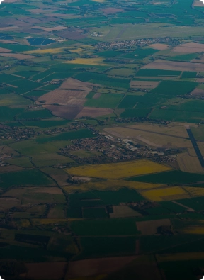 Aerial view of rural farmland and scattered buildings, representing remote area surveillance and rural security patrols by American Security Force.