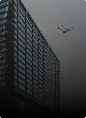 Surveillance drone flying near a modern commercial office building, providing aerial security monitoring by American Security Force.