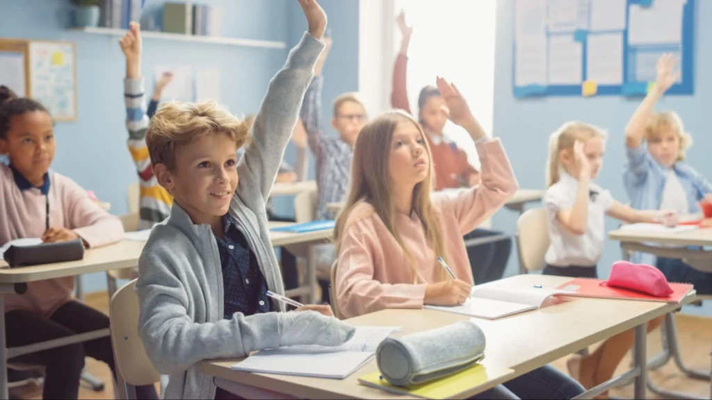 Elementary school students raising hands in a classroom, highlighting the importance of school security guard services for student safety – American Security Force.