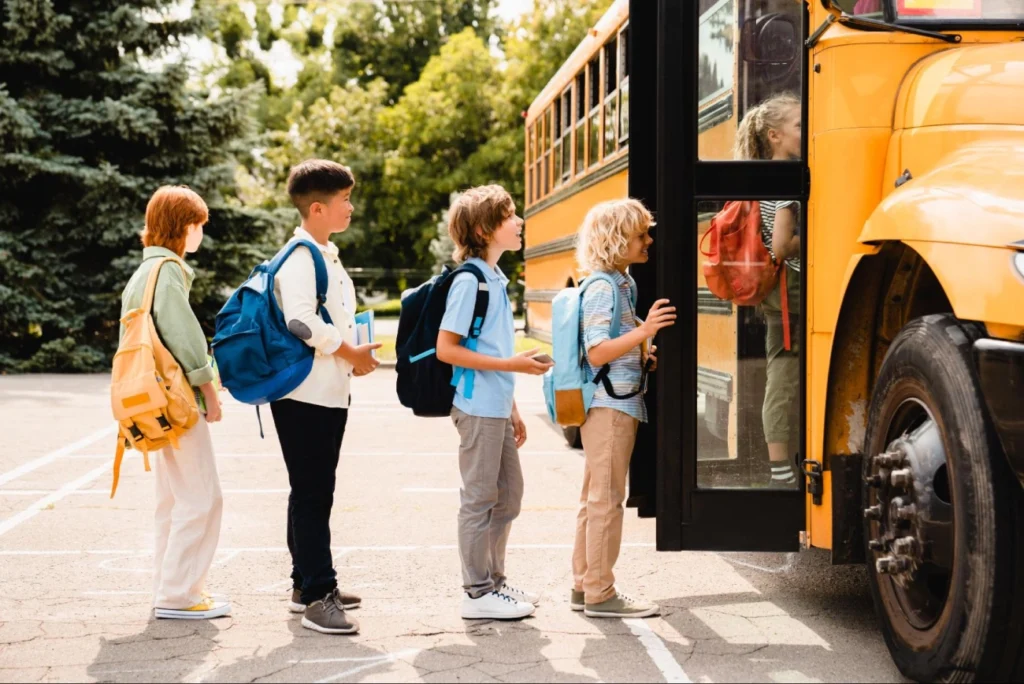 Children boarding a yellow school bus in a safe and orderly line, emphasizing the role of school security guard services in protecting students during transportation – American Security Force.