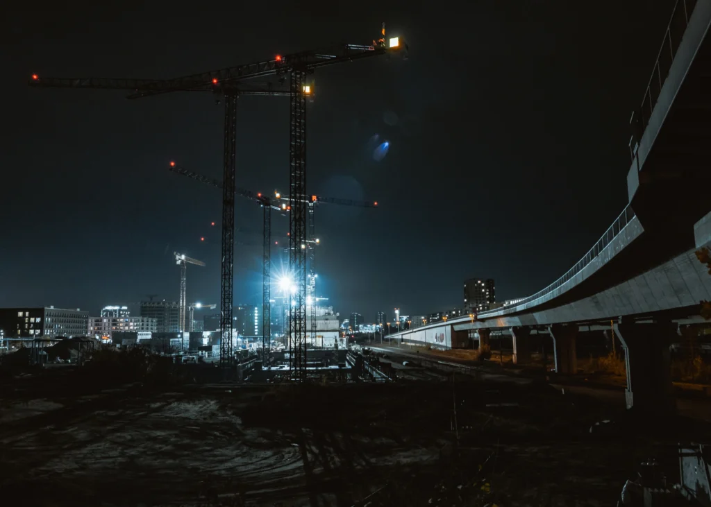 Nighttime construction project with cranes and floodlights, highlighting the importance of 24/7 construction site security plan.