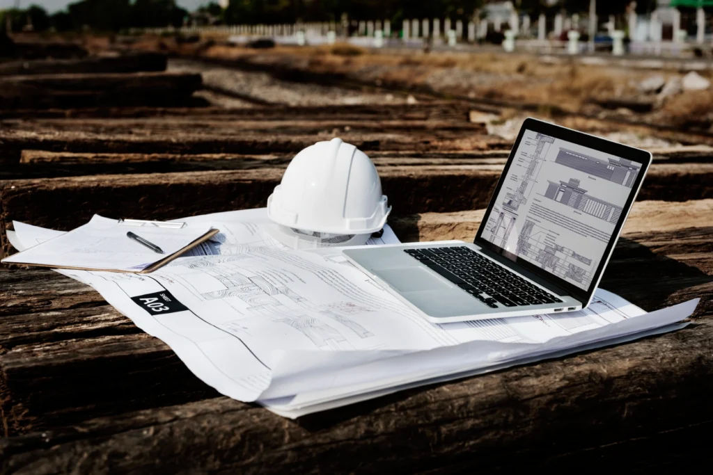 Construction site plans with blueprints, hard hat, and laptop on wooden beams, representing American Security Force's strategic safety approach.
