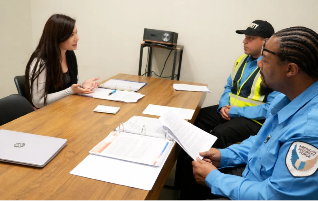 American Security Force supervisor interviewing security guards during hiring or training meeting with documents
